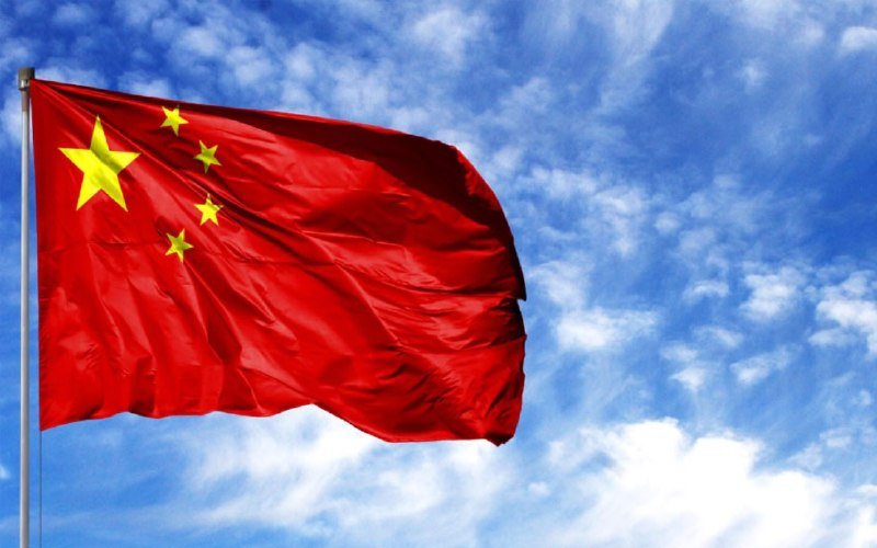 A red flag with five yellow stars waves on a flagpole against a blue sky with scattered white clouds.