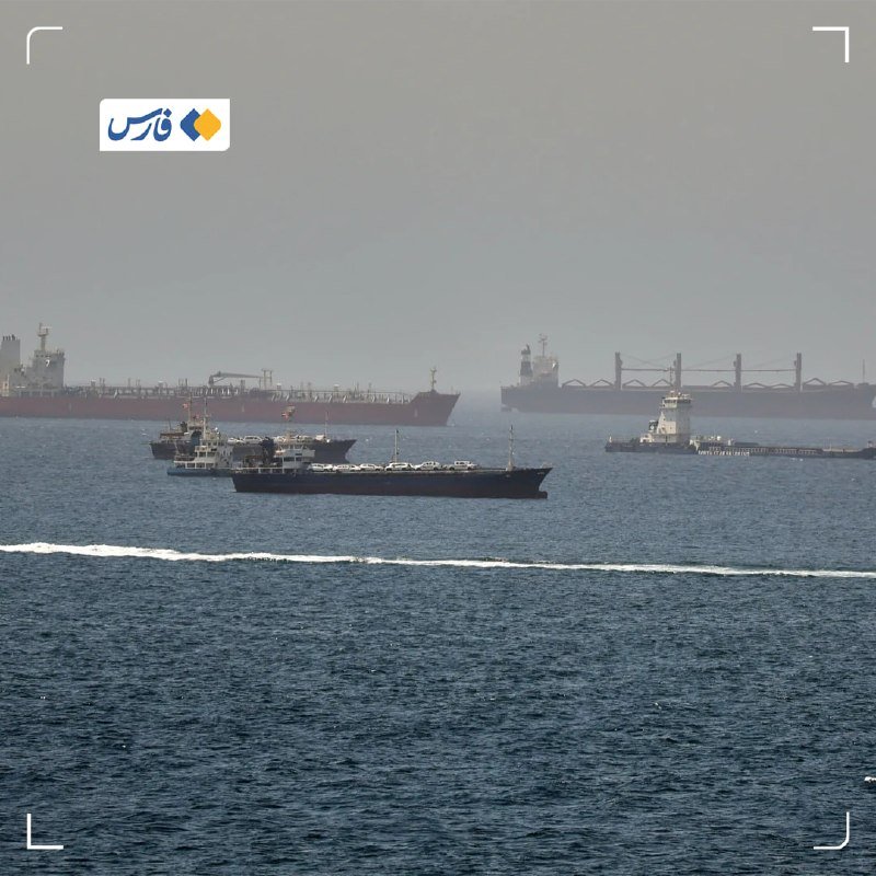 Several large cargo ships, a smaller vessel carrying vehicles, and a tugboat navigate through hazy waters in a busy shipping channel.