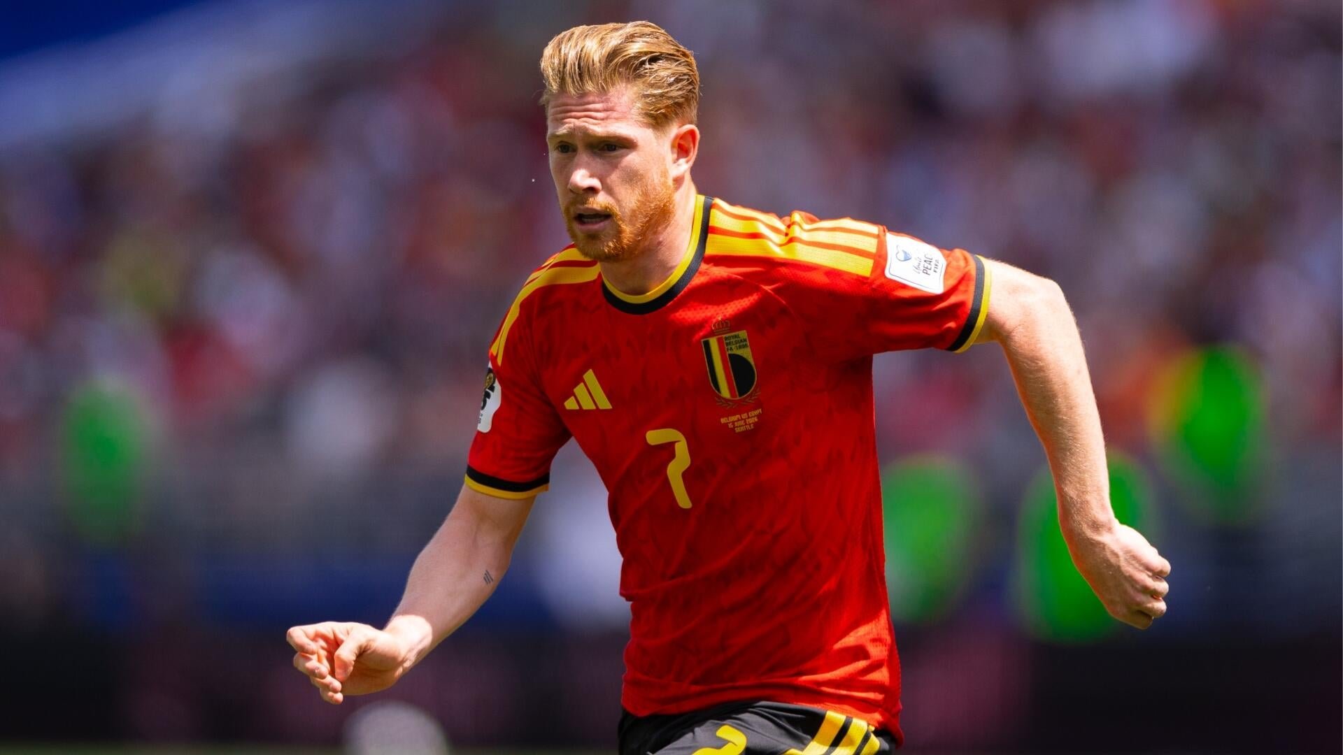 A blonde, bearded soccer player wearing a red Belgium national team jersey with the number 7 runs across the field during a match.