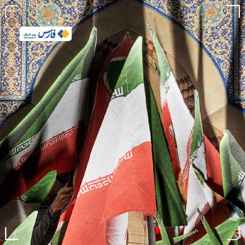 Multiple Iranian flags are held up against an ornately tiled arched ceiling.