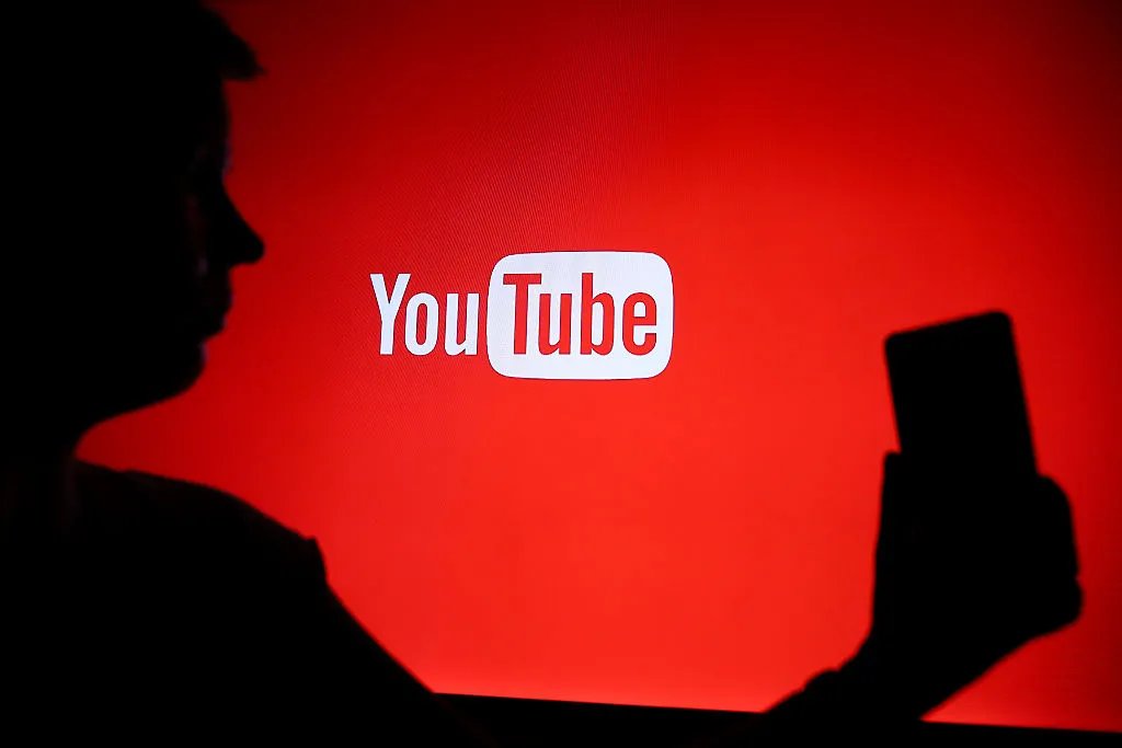 A silhouetted person holds a smartphone in front of a red screen displaying the YouTube logo.