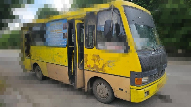 A yellow minibus with a blue side advertisement sits parked with its side door open on a paved area near trees.