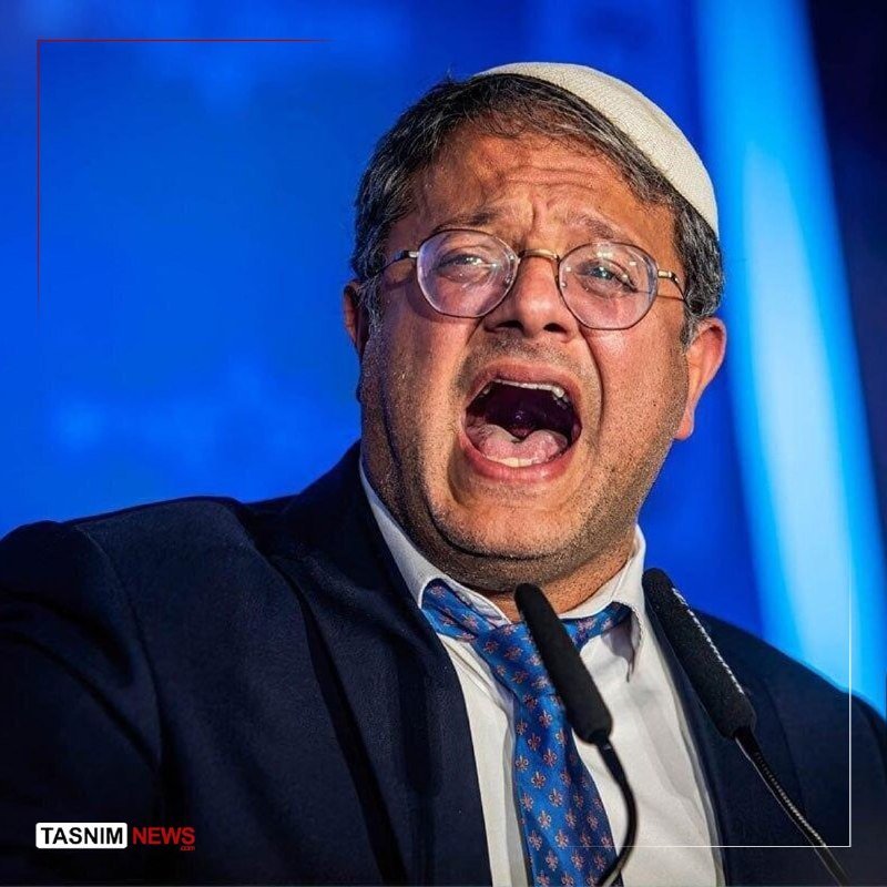 A man in a skullcap, glasses, and blue tie speaks emphatically into a microphone against a blue backdrop, with a "Tasnim News" logo visible.
