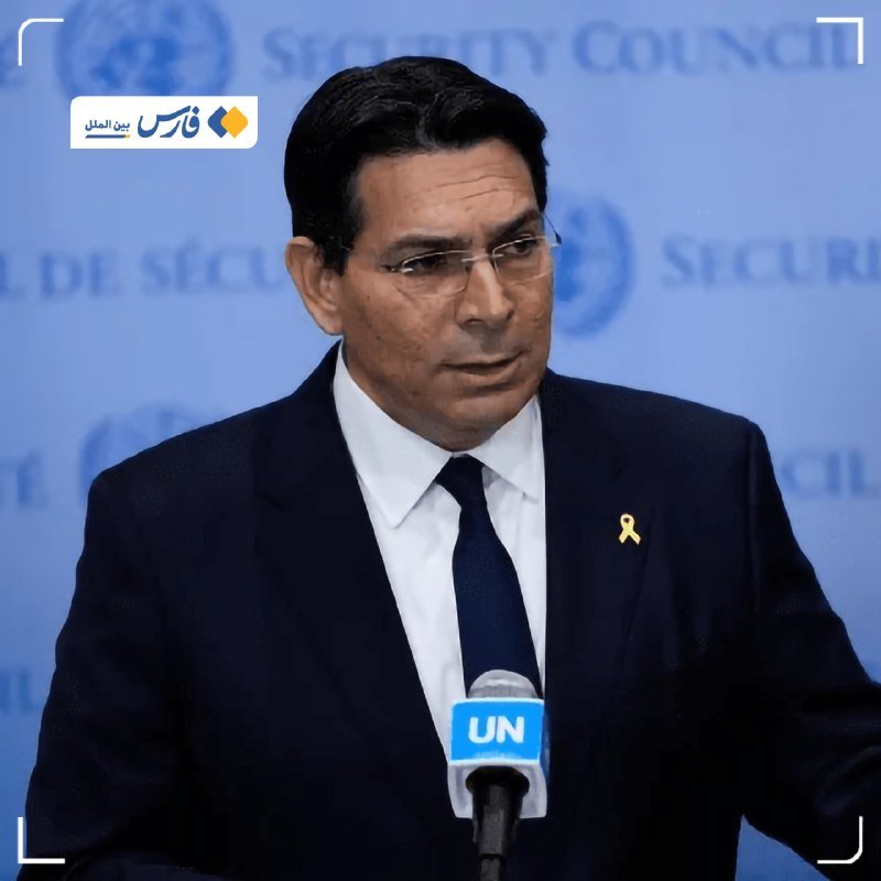 A man in a dark suit, white shirt, blue tie, and yellow ribbon speaks into a "UN" microphone against a blue backdrop displaying "SECURITY COUNCIL" text and the UN emblem.