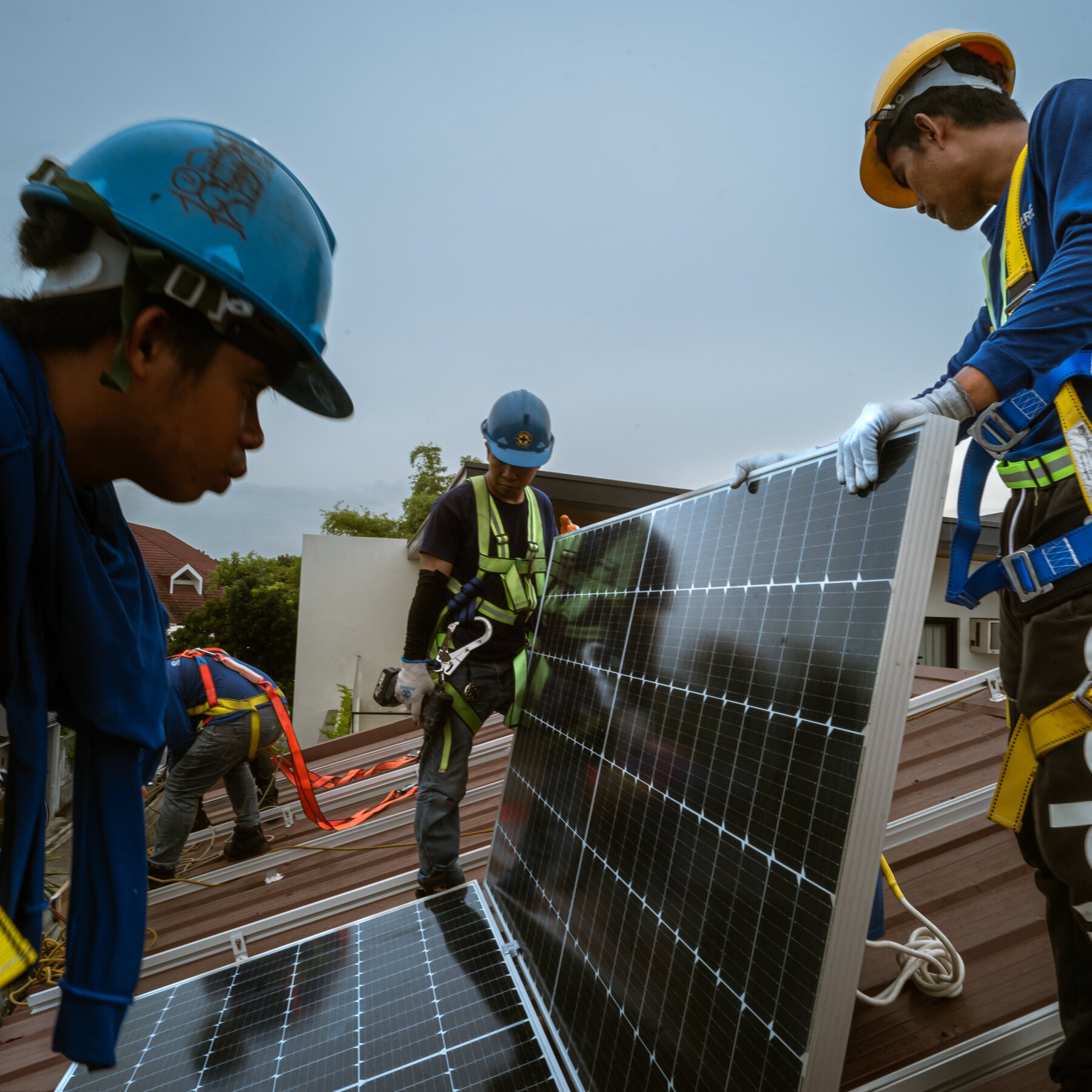 Workers in hard hats and safety harnesses install solar panels on a residential rooftop.
