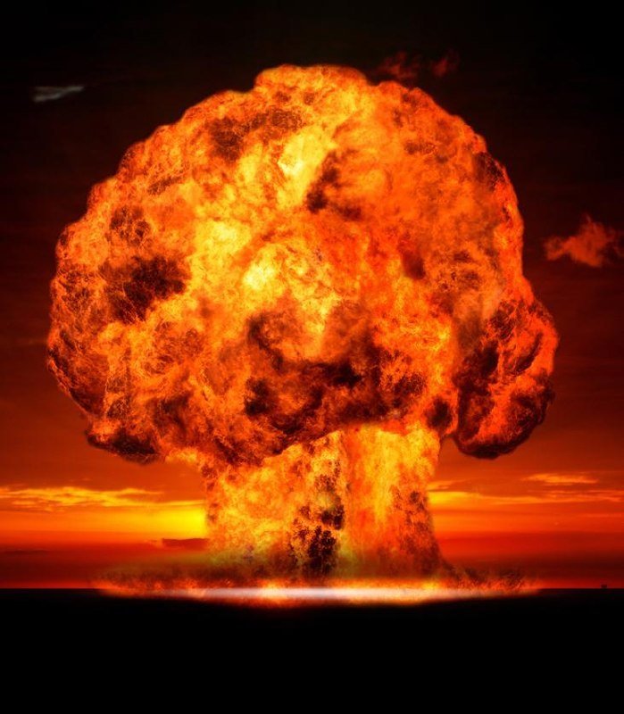 A large mushroom-shaped explosion of bright orange and yellow fire rises against a dark, cloudy sky.