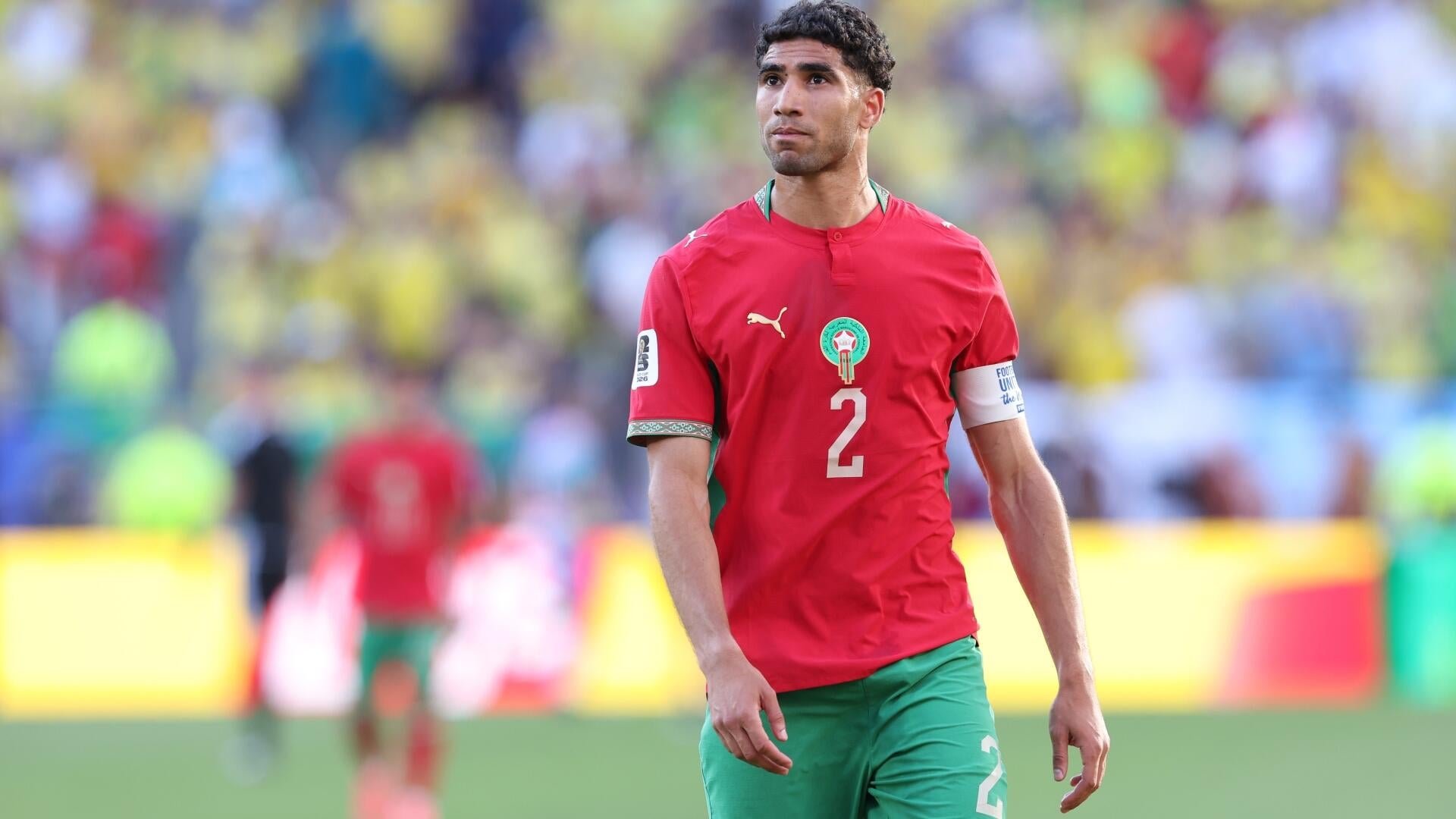 A soccer player wearing a red Morocco jersey with the number 2 and a captain's armband stands on the field during a match.