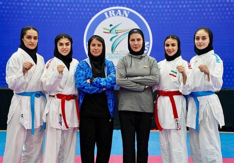 Six women in karate uniforms and hijabs pose with raised fists in front of a blue backdrop displaying the Iran Karate Federation logo.