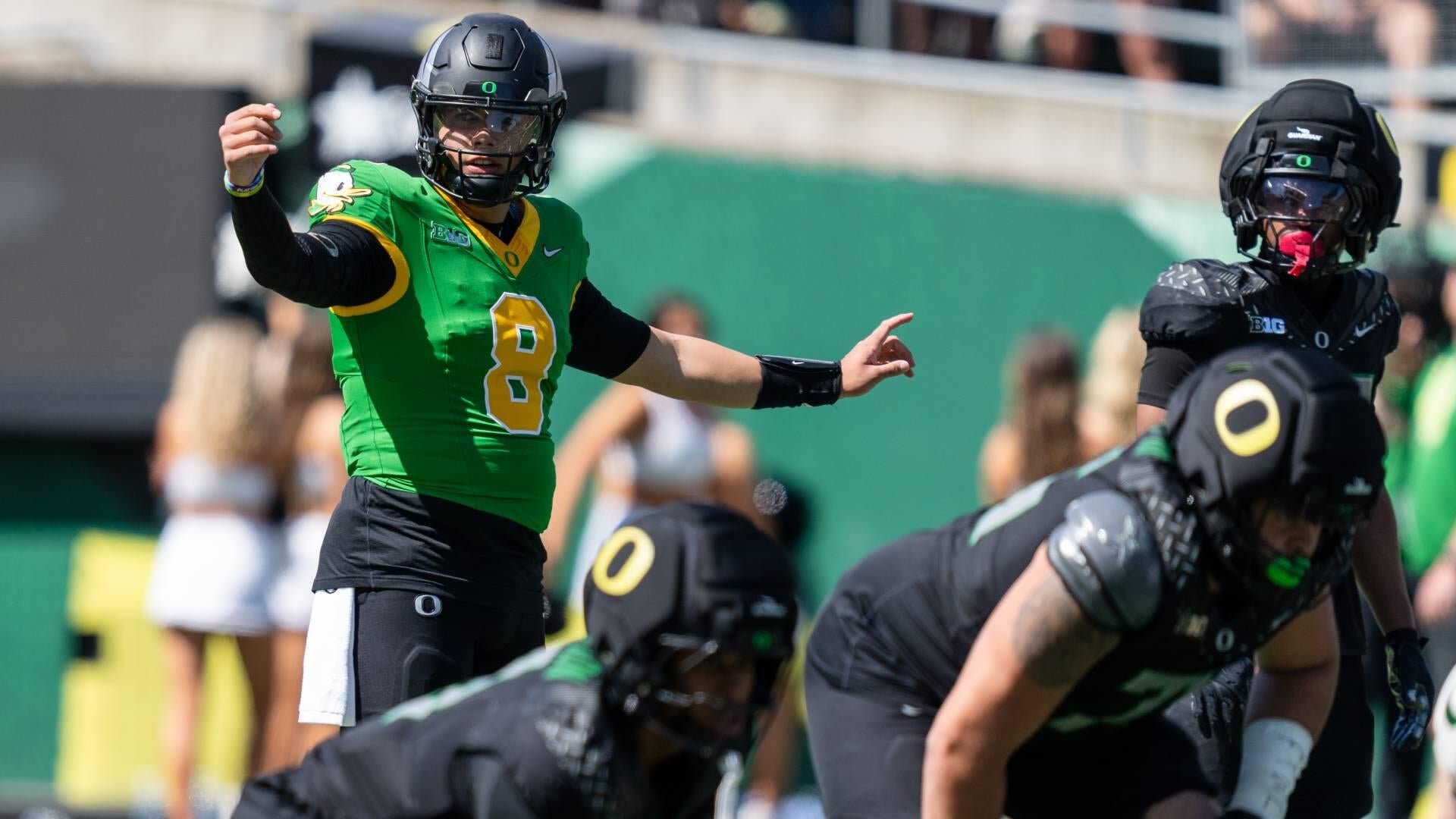 A football player wearing a green jersey with the number 8 calls signals at the line of scrimmage during a game.