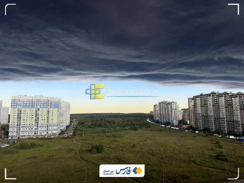 Aerial view of residential apartment buildings flanking a grassy field under heavy dark storm clouds, with "Exilenova +" and "فارس" watermarks visible.