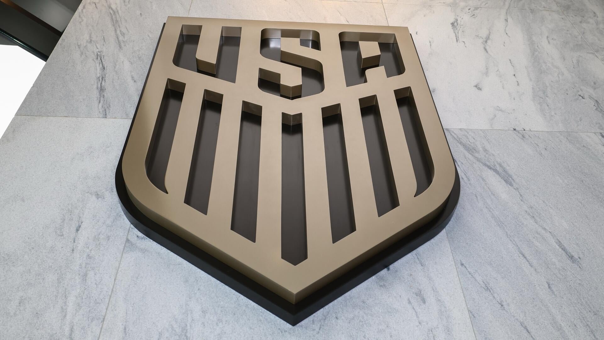 A large, three-dimensional bronze and black shield-shaped sign reading "USF" lies flat on a gray marble floor.