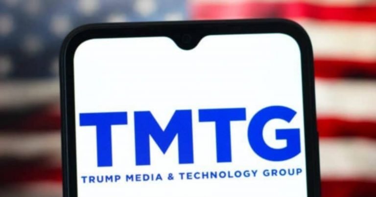 A smartphone displays the blue "TMTG" logo for Trump Media & Technology Group against a blurred American flag backdrop.