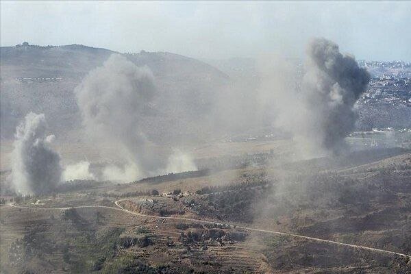 Multiple plumes of gray and white smoke rise from explosions across a hilly, sparsely vegetated landscape with a winding dirt road.