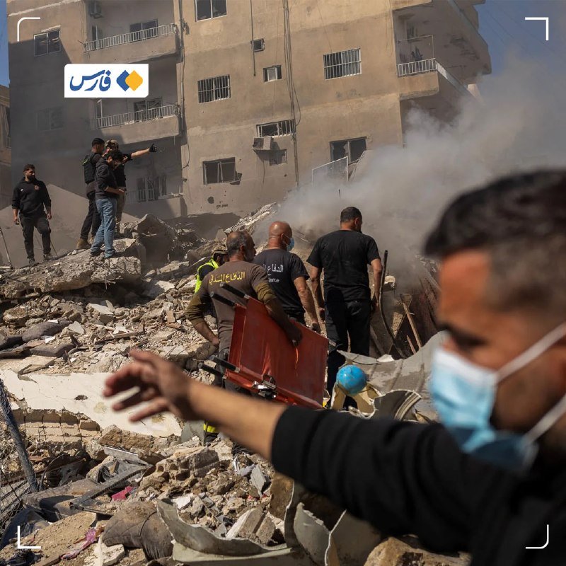 Rescue workers carry a stretcher through concrete rubble amid dust and smoke near a damaged multi-story residential building.