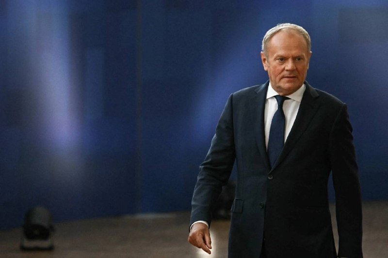 A man in a dark suit and blue tie walks across a stage with a blue-lit backdrop.