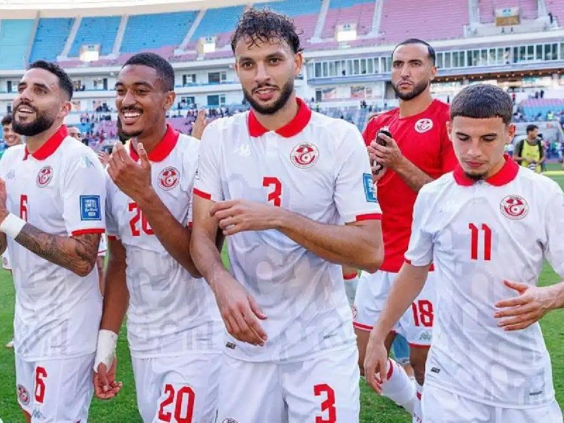 Soccer players in white and red uniforms smile and walk together across a stadium field after a match.