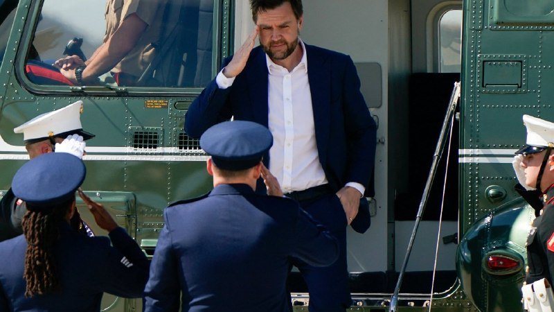 A bearded man in a dark suit exits a green helicopter, saluting uniformed military personnel standing at attention below.