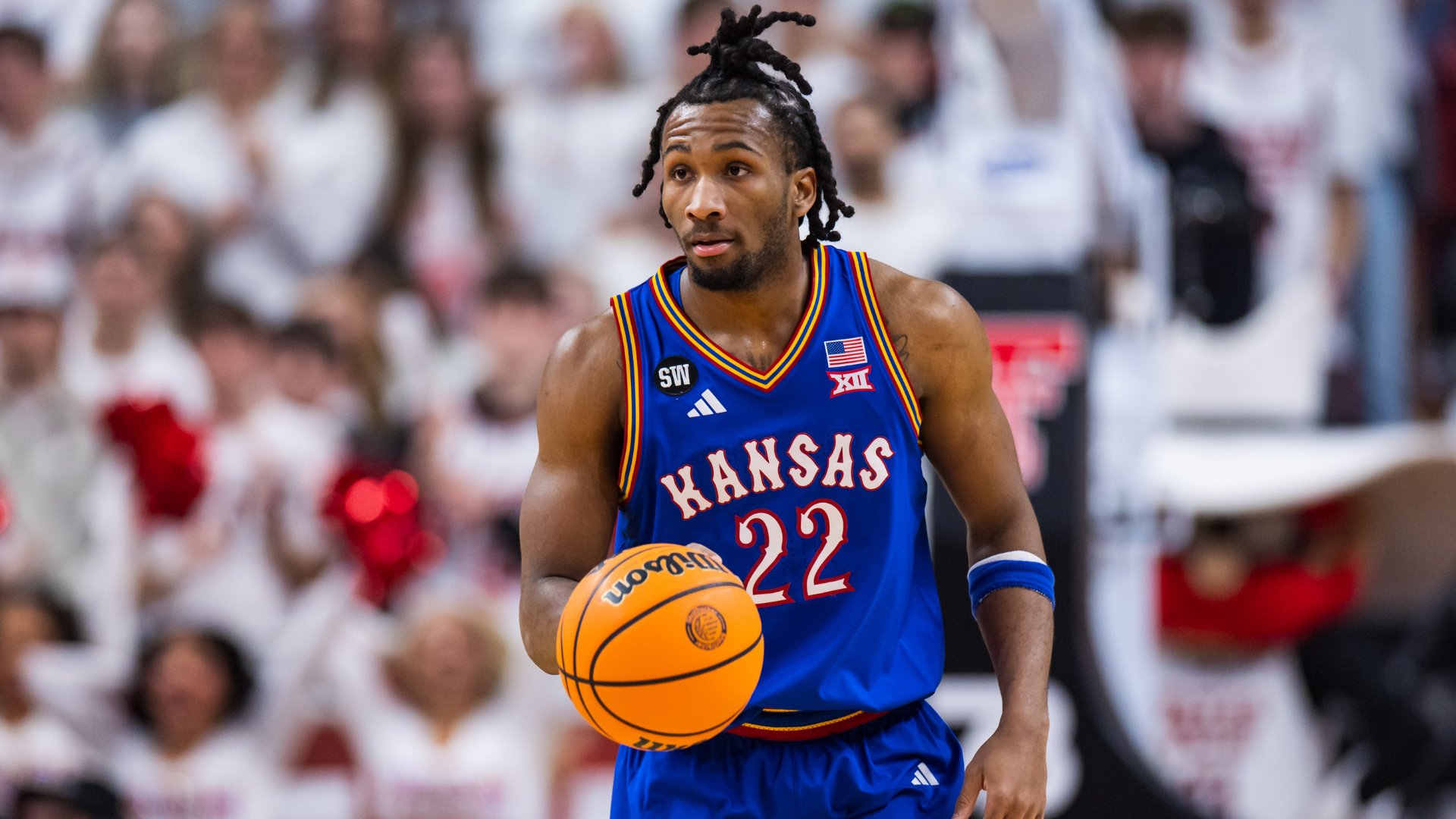 A Kansas basketball player wearing jersey number 22 dribbles a Wilson basketball during a game, with a blurred crowd in the background.