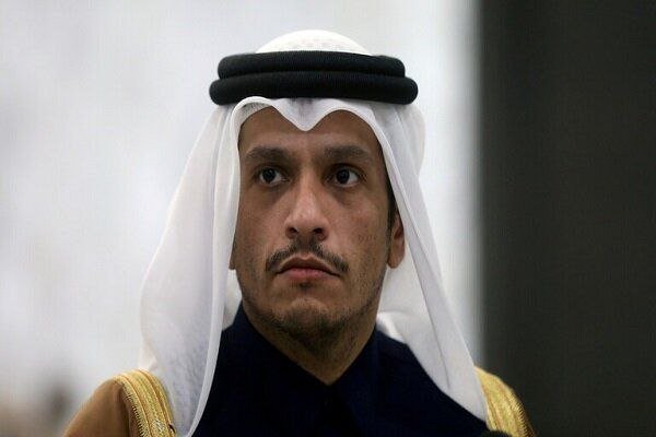 A man wearing traditional Arab headwear (white ghutra with black agal) and a dark garment with gold trim looks off-camera against a blurred background.