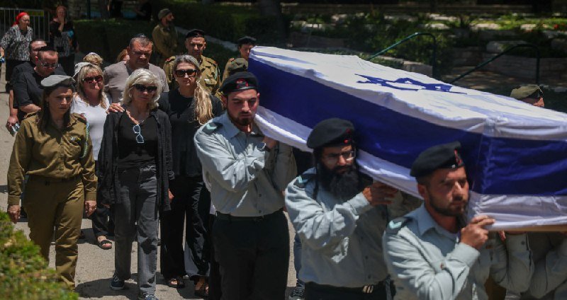 Uniformed soldiers carry a flag-draped coffin outdoors, followed by a procession of mourners in civilian and military attire.