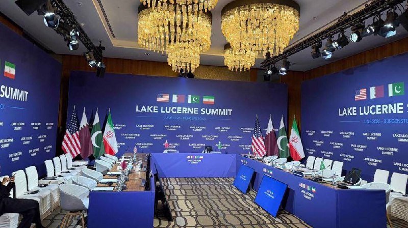 Empty conference room set for the "Lake Lucerne Summit" with U.S., Qatar, Iran, and Pakistan flags displayed behind a head table under ornate chandeliers.