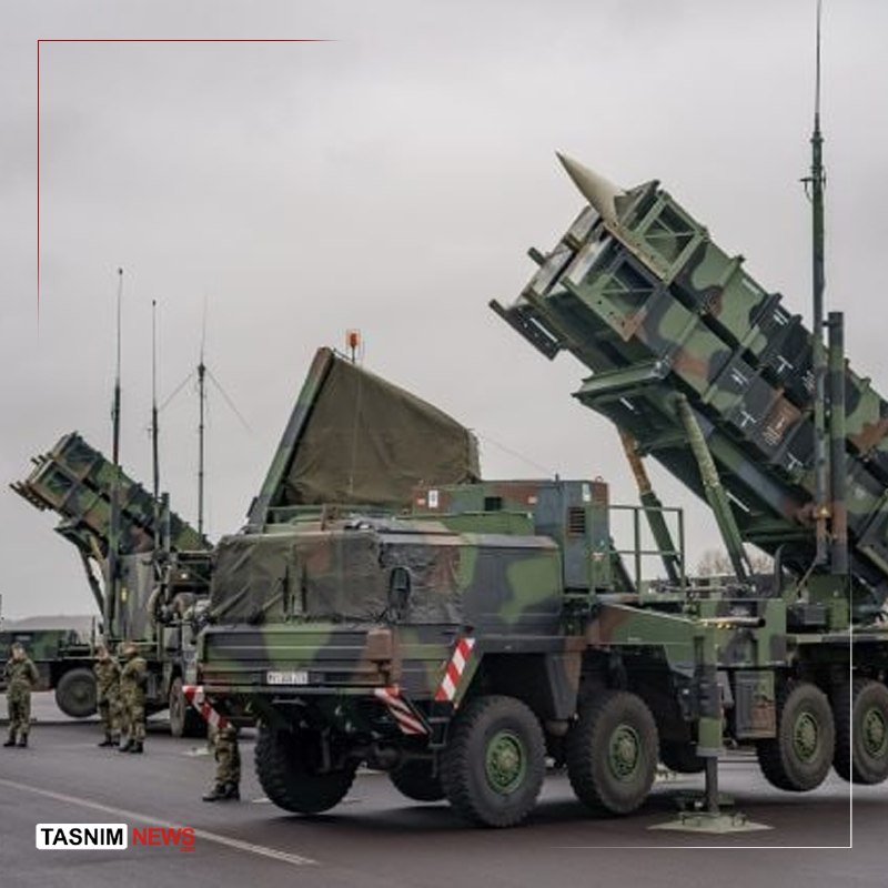 Camouflaged military vehicles carrying elevated missile launcher systems are displayed on a paved surface, with uniformed personnel standing nearby.