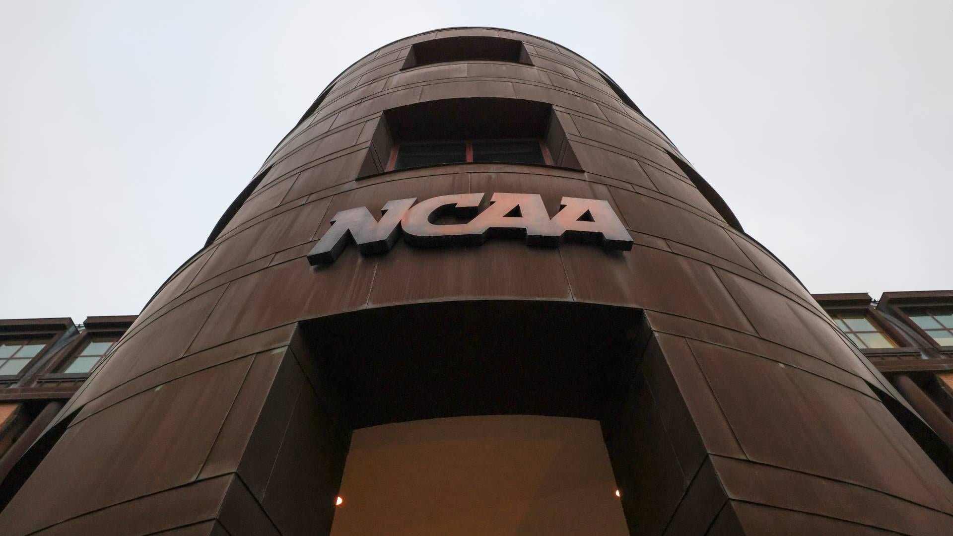 A low-angle view shows the metallic NCAA logo mounted on a tall, brown-paneled building entrance against an overcast sky.