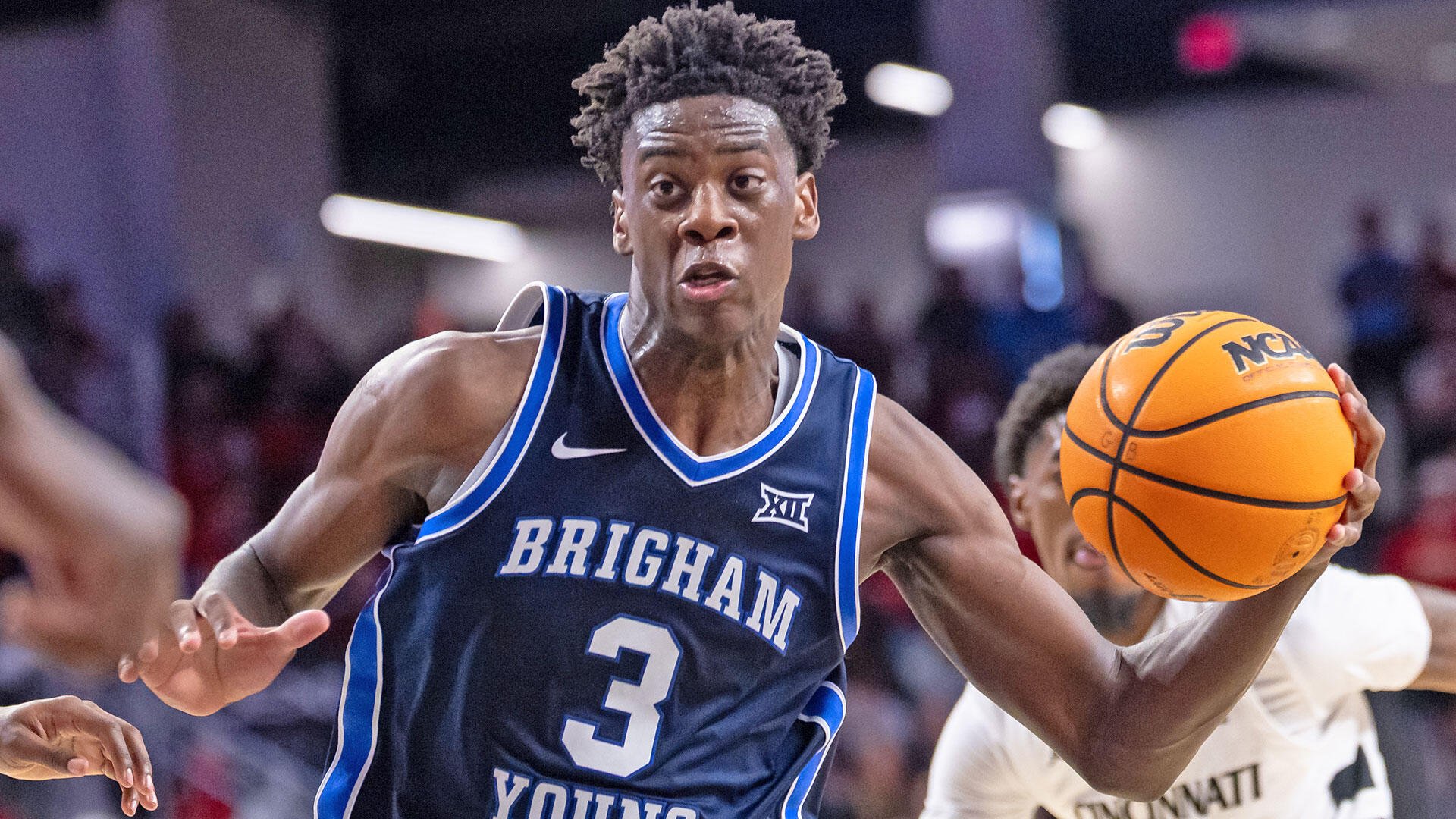 A Brigham basketball player wearing a navy "Brigham Young" jersey numbered 3 drives with an orange NCAA basketball during a game.