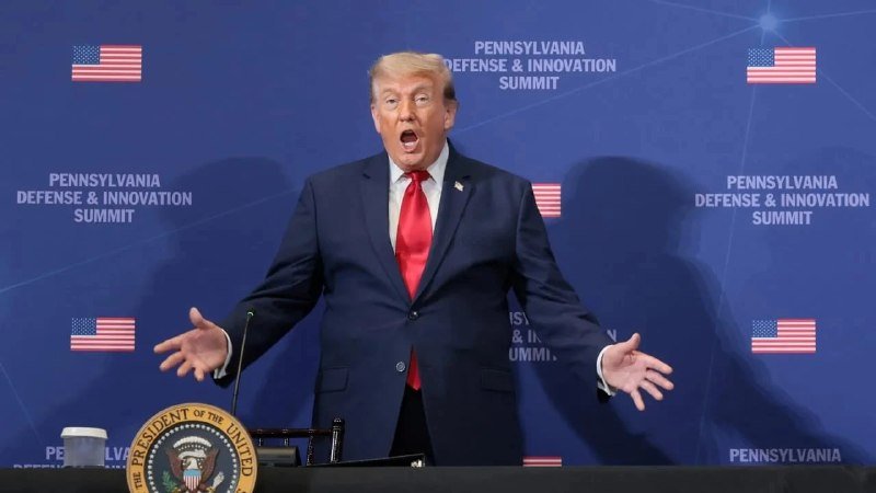 A man in a dark suit and red tie stands at a podium bearing the Presidential Seal, speaking with open arms against a blue backdrop reading "Pennsylvania Defense & Innovation Summit."