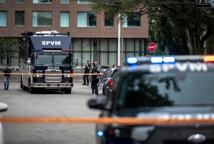 Police vehicles marked "SPVM" and officers stand behind yellow tape near a building during an active scene.