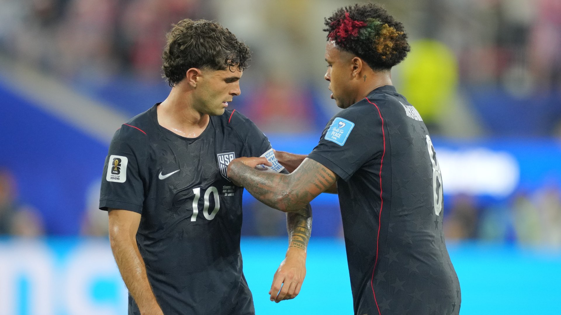 Two USA soccer players in black jerseys, one wearing number 10, stand face-to-face on the field during a match.