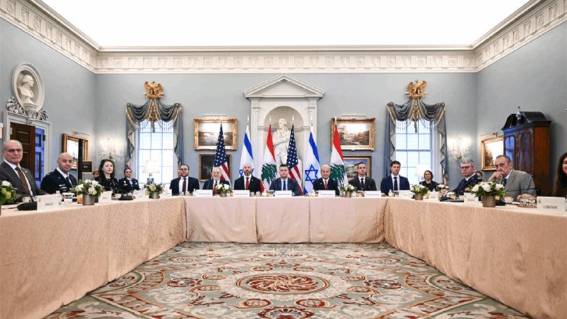 Officials seated at a U-shaped table face the camera in an ornate blue room, with U.S., Lebanese, and Israeli flags displayed in the center background.
