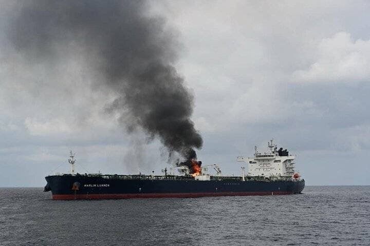 A large tanker labeled "MARLIN LEGAZPI" is engulfed in flames on the open sea, with thick black smoke billowing into the cloudy sky.