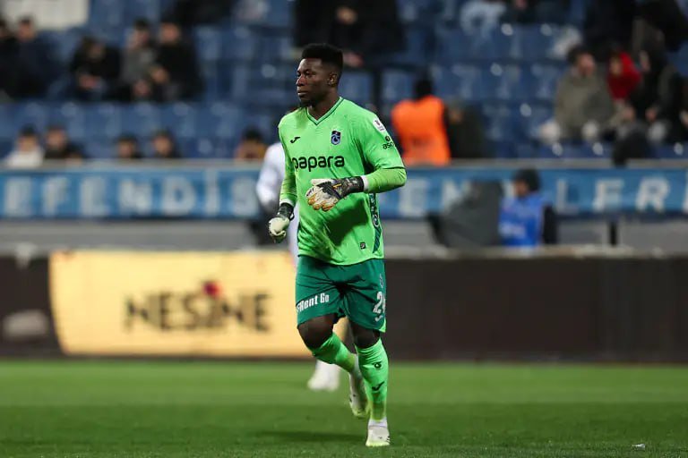 A soccer goalkeeper in a bright green uniform with "Napara" printed on the chest runs across the grass field, wearing gloves, with stadium seats and spectators visible in the background.