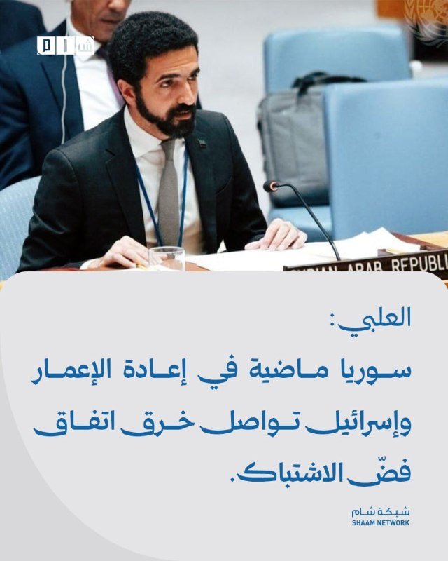 A bearded man in a suit speaks at a desk with a microphone, accompanied by Arabic text and the Shaam Network logo.