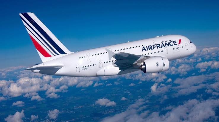 An Air France double-decker passenger jet flies above scattered clouds in a clear blue sky.