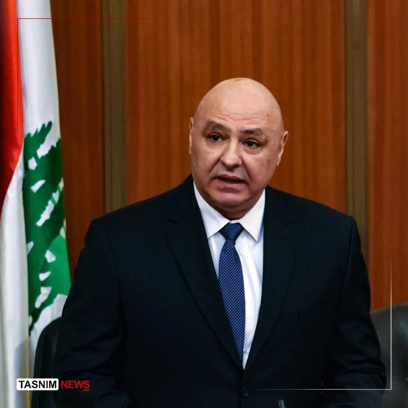 A bald man in a dark suit and blue tie stands speaking, with a red, white, and green flag visible behind him; a "Tasnim News" watermark appears at the bottom left.
