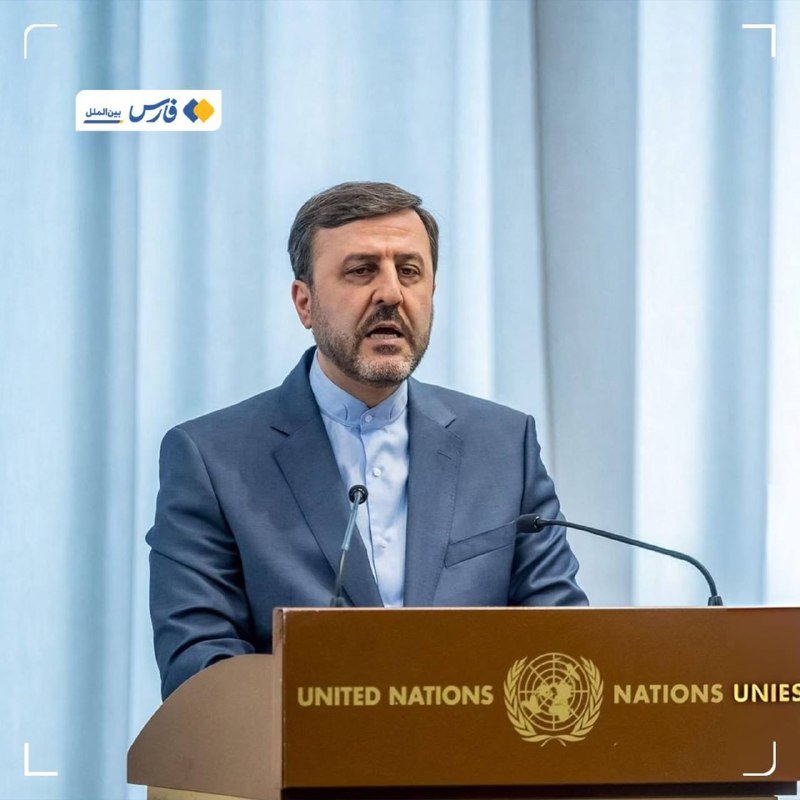 A bearded man in a blue suit speaks at a podium bearing the United Nations emblem, with light blue curtains behind him.