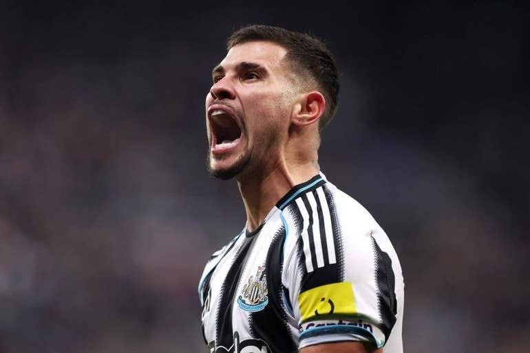 A bearded soccer player in a black-and-white striped jersey with a yellow captain's armband shouts passionately with his mouth wide open during a match.