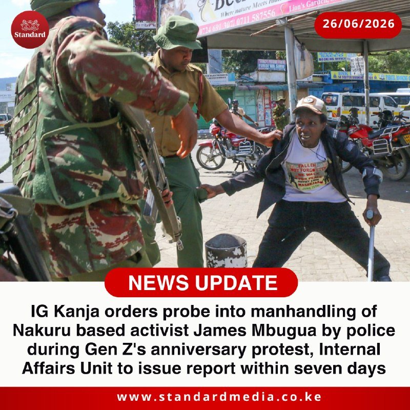 A uniformed police officer and an armed soldier physically restrain a protesting man wearing a protest T-shirt on a street with motorcycles and shop signs in the background.