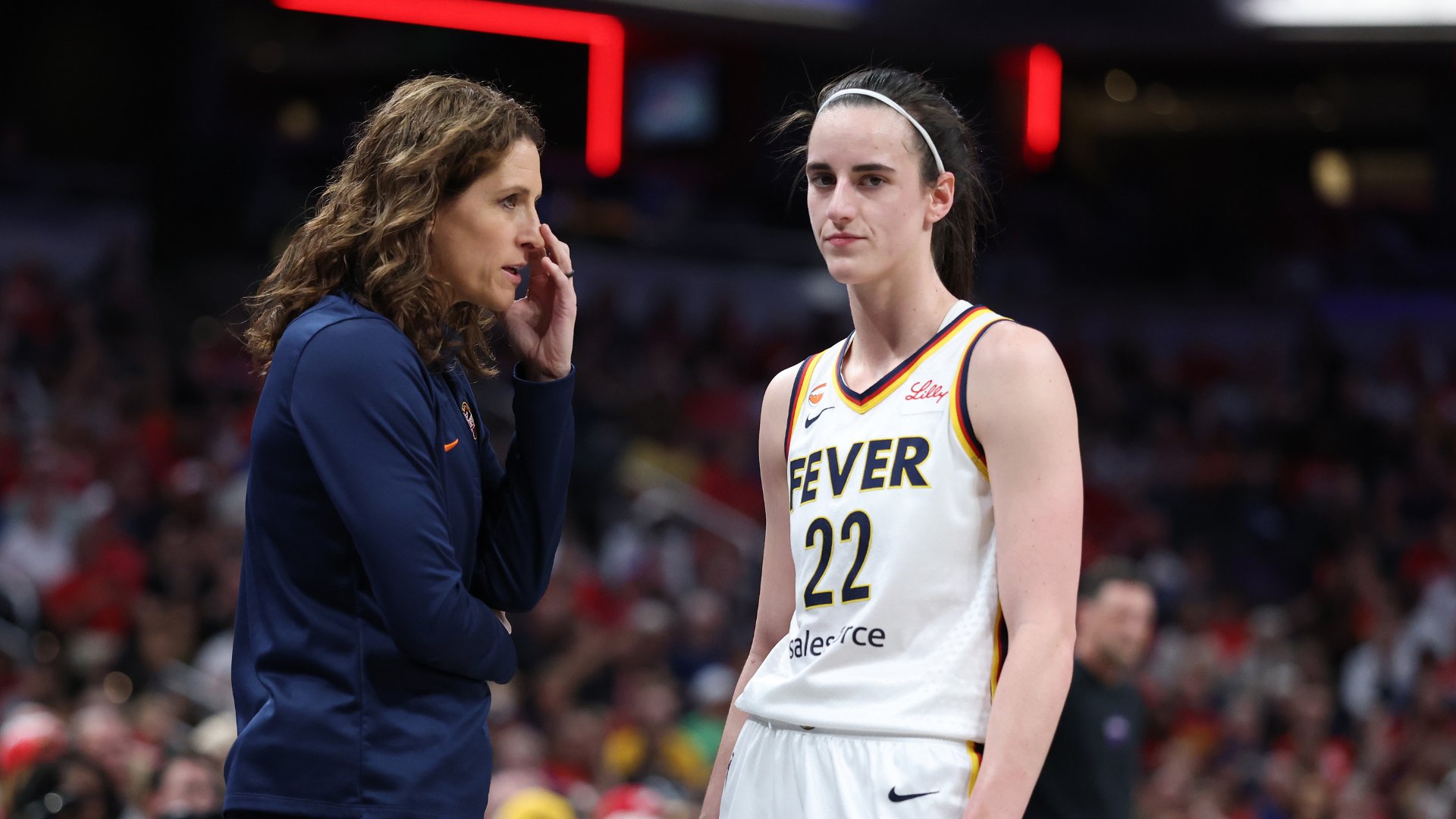 A woman in a navy pullover speaks to a basketball player wearing a white "Fever" jersey with the number 22 on a court.