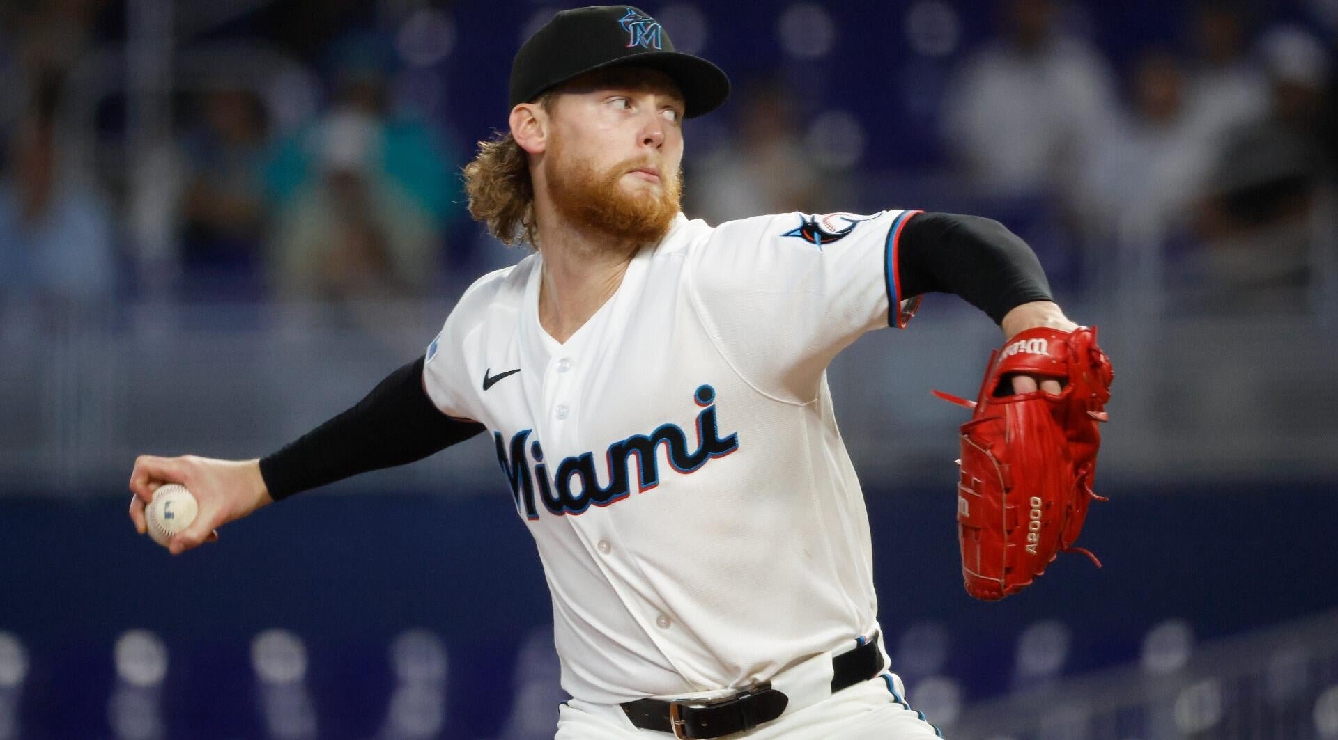 A bearded Miami Marlins pitcher with long hair throws a pitch during a game, wearing a white jersey and red glove.