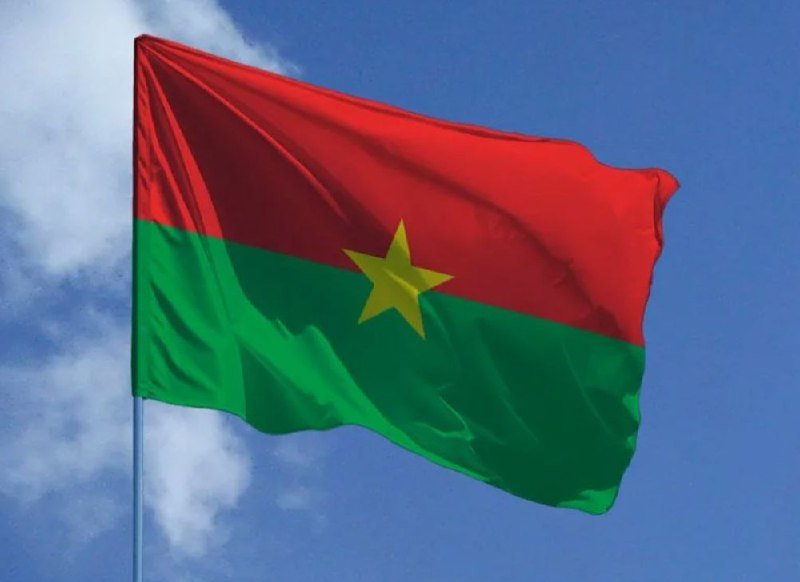 A red and green flag with a yellow star waves against a blue sky with scattered clouds.