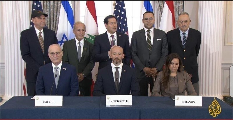 Eight officials in suits pose behind a table with nameplates reading "Israel," "United States," and "Lebanon," with Israeli, American, and Lebanese flags displayed behind them.