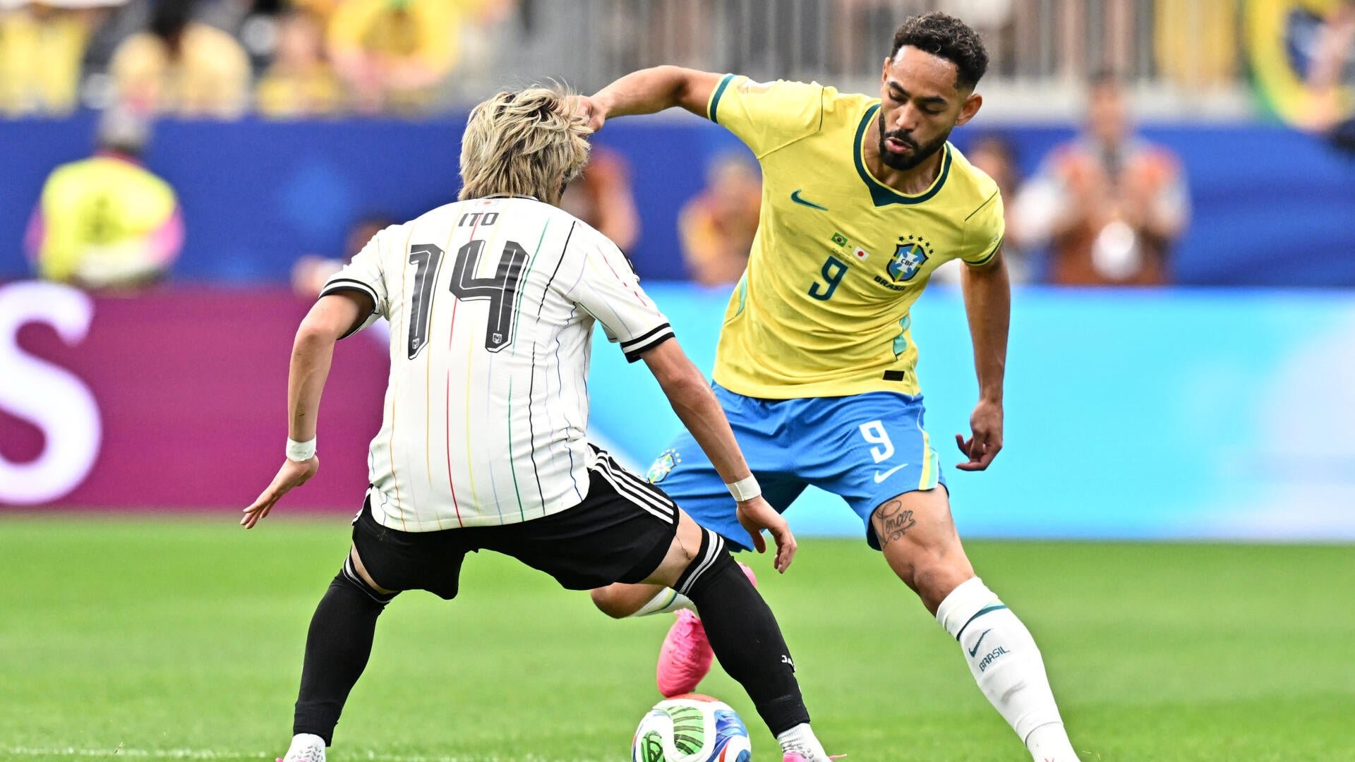 Two soccer players compete for the ball during a match, one in a yellow jersey with number 9 facing a player in a white striped jersey marked 14, name "ITO" visible above.