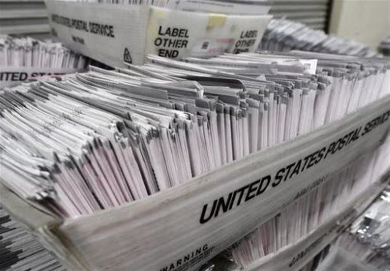 A bin labeled "UNITED STATES POSTAL SERVICE" is filled with stacks of white envelopes, with a nearby container marked "LABEL OTHER END."
