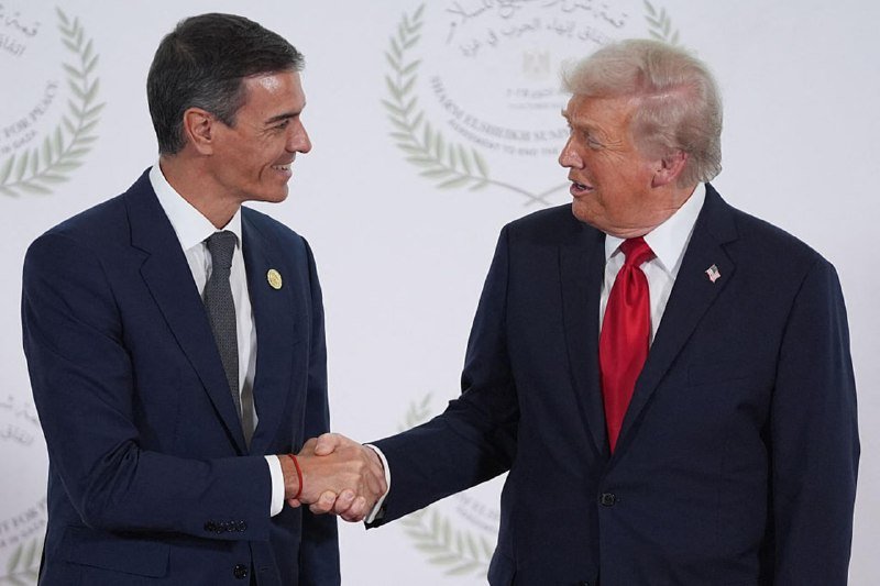 Two men in dark suits smile and shake hands in front of a backdrop featuring the "Forum Élargi de la Méditerranée" emblem and text.