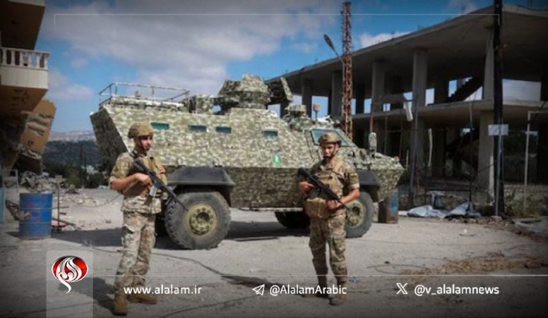 Two armed soldiers in camouflage uniforms stand in front of a camouflage-patterned armored vehicle on a debris-strewn street near damaged buildings.