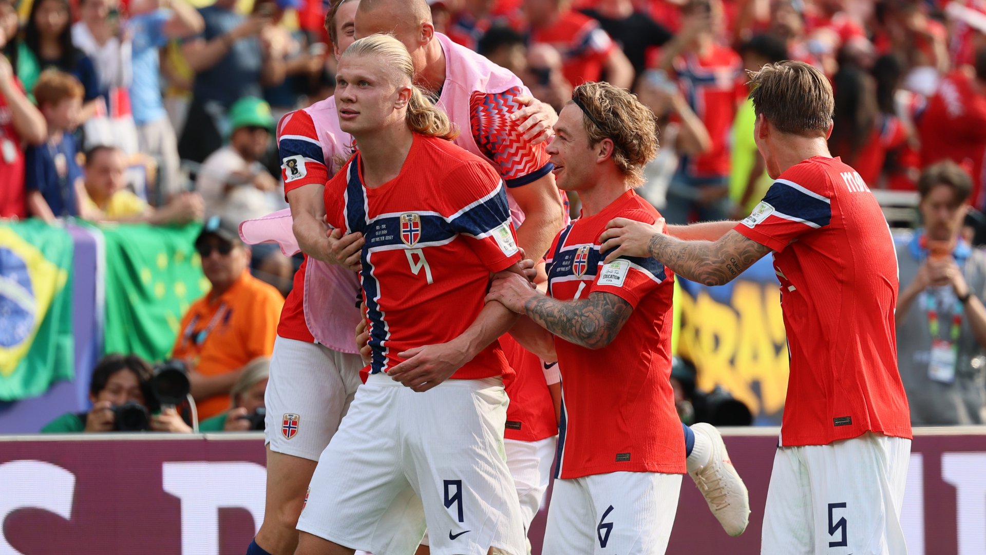 Soccer players in red Norway jerseys celebrate on the field in front of a cheering crowd in a stadium.