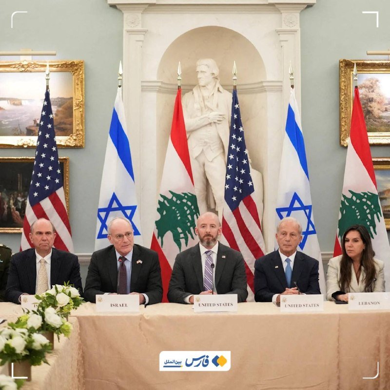 Five officials sit at a table labeled "Israel," "United States," and "Lebanon," flanked by American, Israeli, and Lebanese flags, with a statue of George Washington behind them.